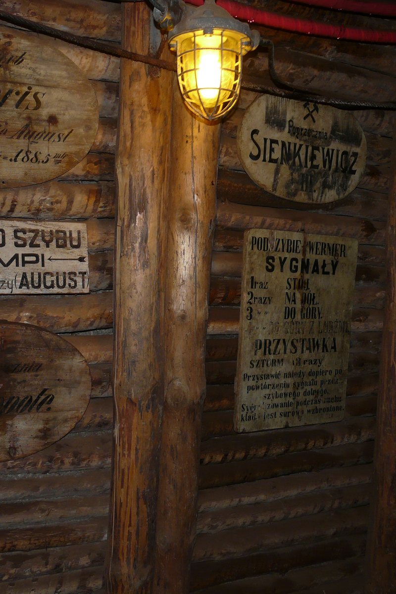 Historic timbered gallery deep inside the Bochnia Salt Mine, lit by a miner's lamp, with original wooden shaft signs.